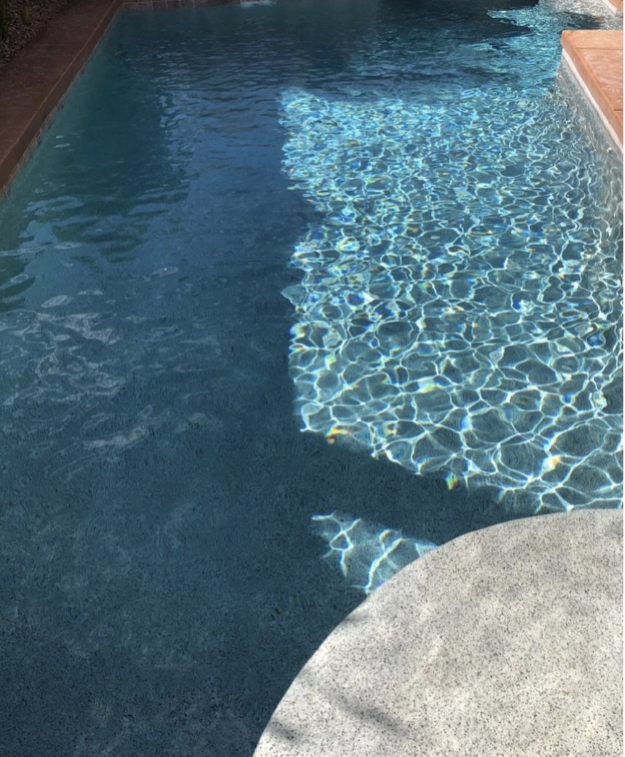 Clear pool water with sunlight reflections and concrete step edge